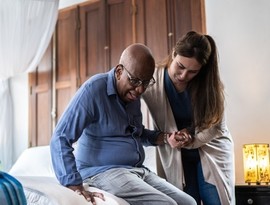 Home caregiver helping a senior man standing up at home